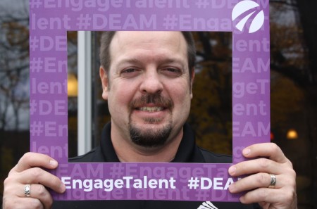 A man holds a picture frame around his face. Text reads: Engage Talent