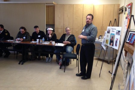 A man stands in front of Bristol board presentations and talks to a room of seated adults. 