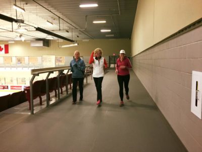 Three adults walking on an indoor walking track that wraps around an arena ice surface