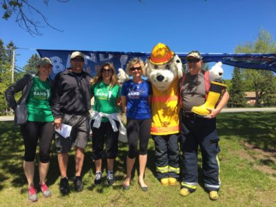 Four adults, three of whom are wearing Band on the Run T-Shirts, pose with a firefighter and a costumed mascot
