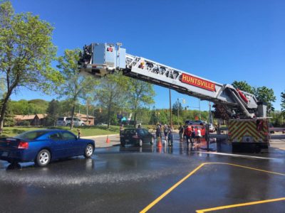 A fire truck extends its bucket lift to rain down water on a passing car at a charity car wash.