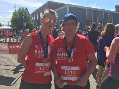 Two people who have finished a foot race pose for the camera wearing finisher medals draped around their necks.