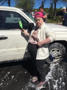 A volunteer poses for the camera while washing a vehicle during a charity car wash.