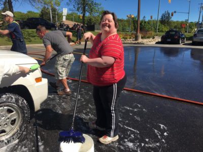 A volunteer poses for the camera while washing a vehicle during a charity car wash.