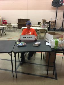 A man in a Band on the Run T-shirt sits at a table holding a sign that reads: VIP Only.