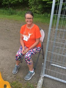 A woman in a Band on the Run T-shirt, athletic pants and running shoes smiles at the camera while seated in a chair.