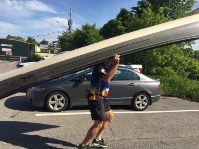 A man carries a canoe by balancing it on his shoulders while traversing the race route.