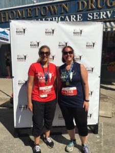 Two women with race finisher medals pose for the camera in front of a white photo backdrop.