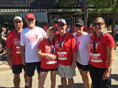 Six people in red and white T-shirts post for the camera. Four of them have race finisher medals.