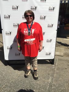A women in a red Band on the Run T-shirt poses with her finisher medal in front of a white photo backdrop.