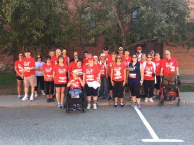 Roughly 30 people, including two with mobility devices, all wear red Band on the Run T-shirts and pose for a group photograph together.