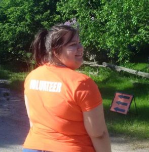 A woman looks over her shoulder to the camera. The back of her orange T-shirt reads: volunteer.