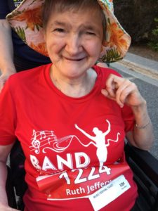 A close-up photo of a women in a floral hat smiling at the camera. She is wearing a red Band on the Run T-shirt.