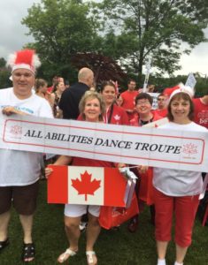 A small group of people in red and white hold a sign that reads: All Abilities Dance Troupe
