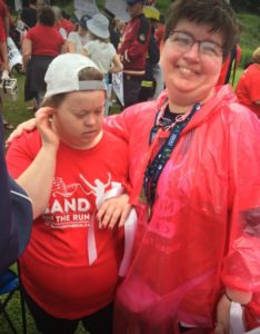 A woman in a red rain poncho puts her arm around the shoulders of a young person, who is wearing a red and white T-shirt.