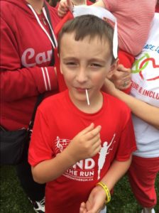 A close u of a boy in a red and white T-shirt enjoying a candy sucker