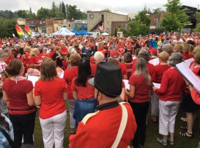 A large crowd of hundreds of people in red and white gathered in a downtown Huntsville park. The photo is taken from behind the crowd.