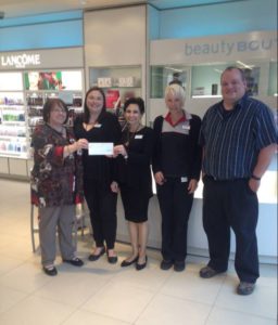 Image shows four women and one man standing in the fragrance section of a Shoppers Drug Mart. Two women are holding a white cheque.