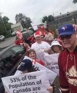 Roughly a dozen people wearing red and white walk by the camera. One person is holding a sign that reads: 53 per cent of the population of Canada are affected by disabilities.