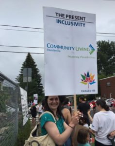 A woman holds a sign that reads: Inclusivity, Community Living Huntsville, Canada 150