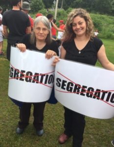 Two women hold signs that show the word "segregation" crossed out with red ink