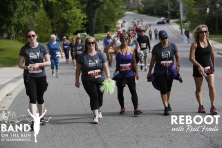 Dozens of people in athletic wear walk on a paved road. One woman has two fingers raised toward the camera in a sign of happiness.