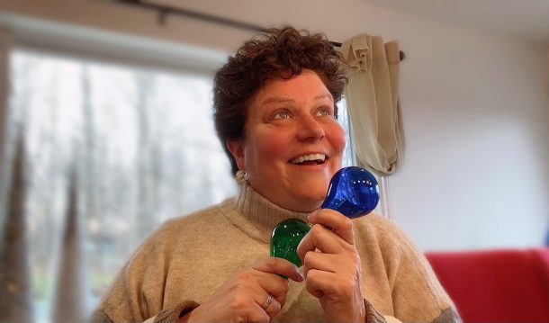 Image shows a smiling, joyful woman looking off into the distance while holding one blue and one green lightbulb. Both lightbulbs are unlit.