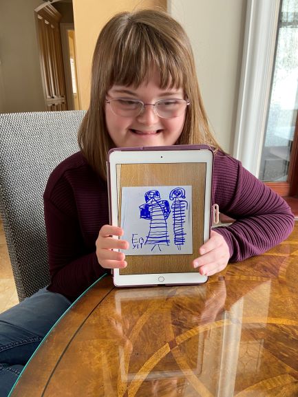 Image shows a smiling teenage girl showing the screen of an iPad to the camera. The screen shows a photo of one of her hand-drawn dress designs made in blue ink on white paper.