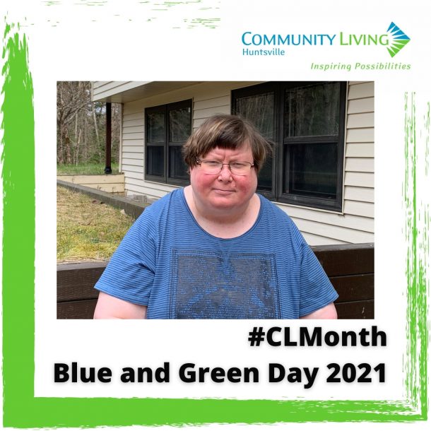 A woman in a blue shirt stands outside with green grass behind her