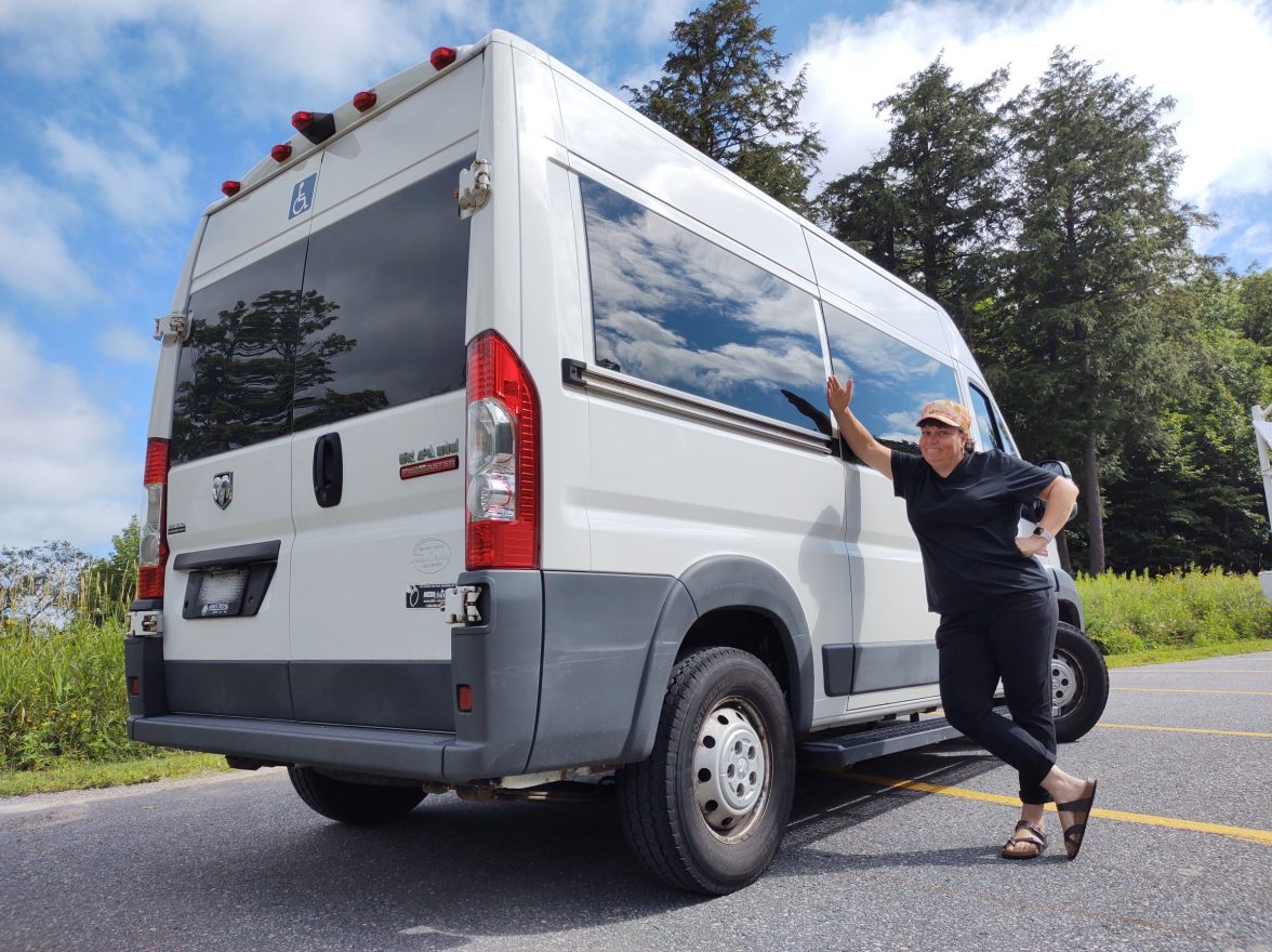 Woman stands beside large white van.