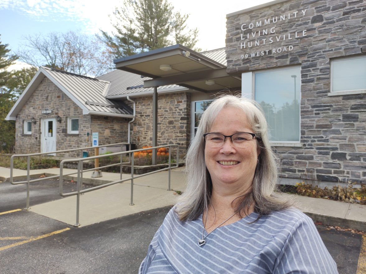 A smiling woman stands in the parking lot in front of a building. Text on building reads: Community Living Huntsville.