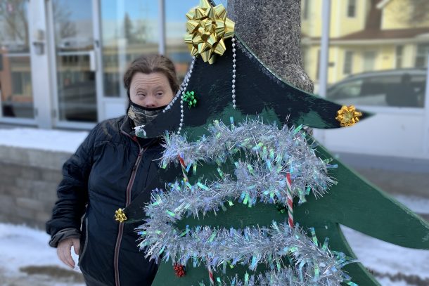 A photo of a woman standing outside beside a decorative wooden Christmas tree.