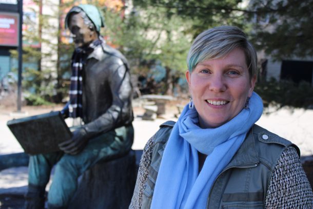Suzanne Willett smiling in Huntsville Civic Square beside a local landmark statue of Tom Thomson.