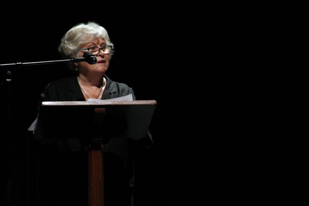 Heather Hunter at a podium under a spotlight on the Algonquin Theatre stage.