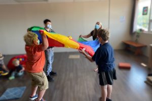 3 kids and an adult playing indoors with a colourful parachute.