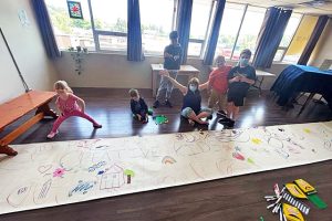 5 children and 1 adult stand or sit around a large paper banner covered in colourful drawings that reads: creative kids.