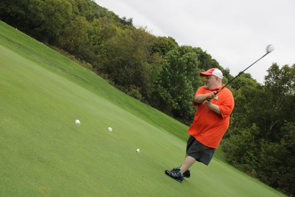 A man on a golf green swings his club at a large white marshmallow.