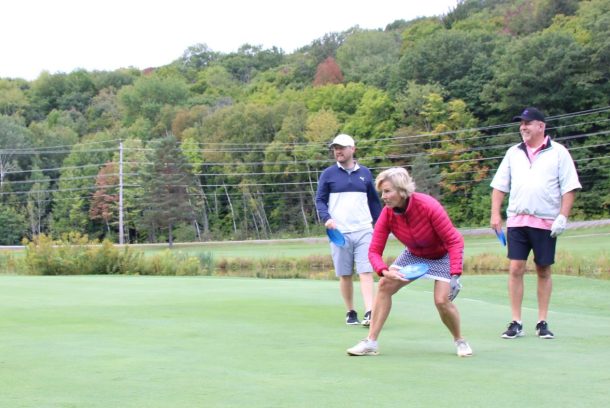 A woman readies to through a blue Frisbee toward the hole on a golf green.