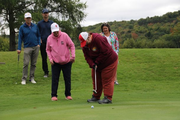 A woman putts a golf ball on a golf green while 4 spectators watch.