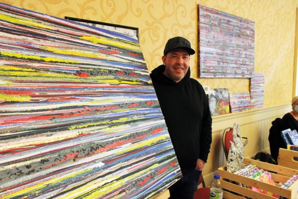 A man stands beside an abstract painting of multicoloured horizontal lines.