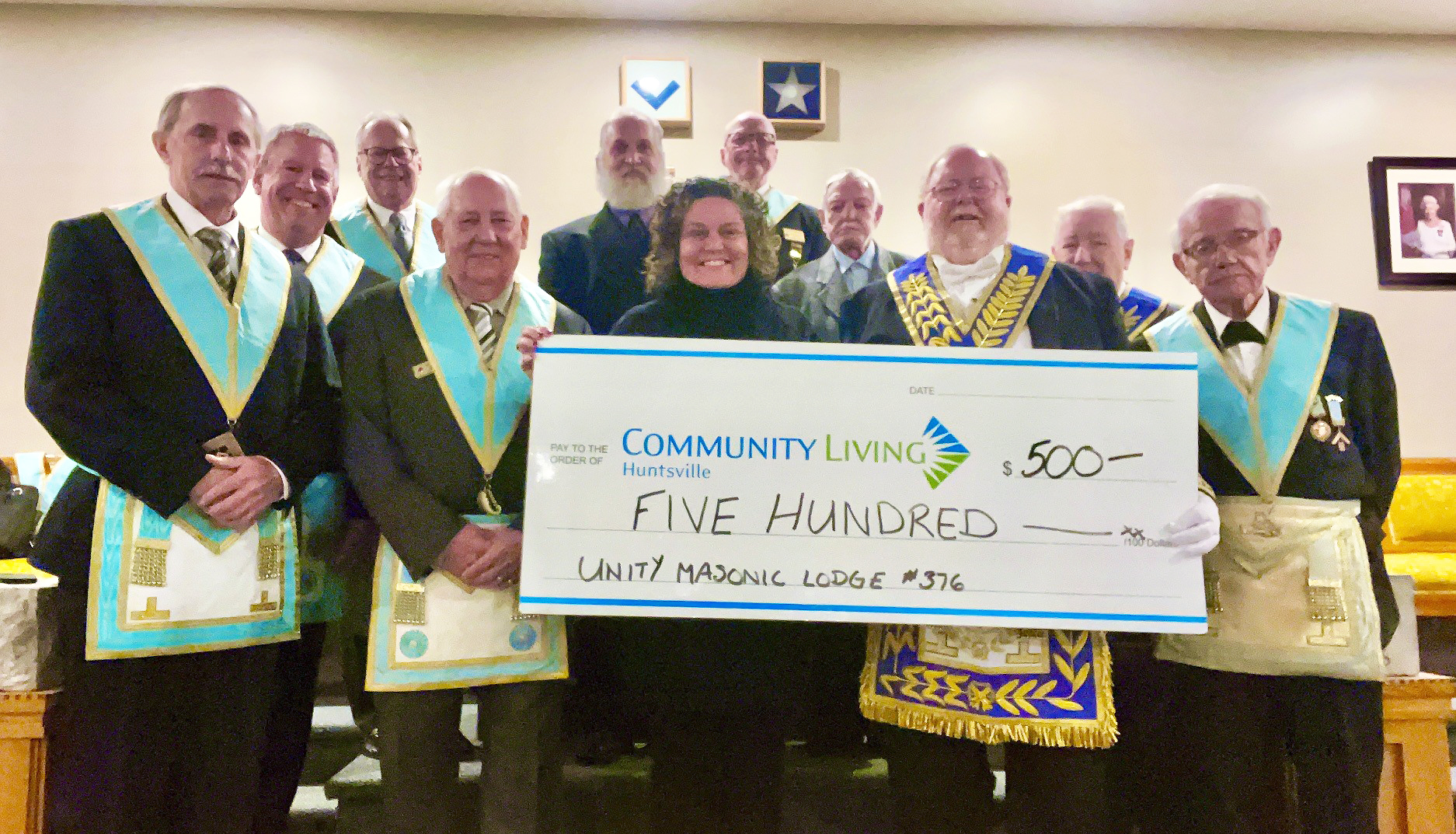 A group of Masonic Lodge members present a Community Living Huntsville staff member with a large novelty cheque for $500