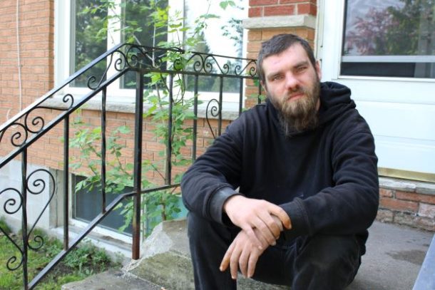 Man in black sweater sits on front stoop of red-brick house