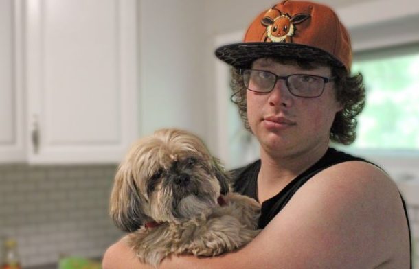 Young man holds small dog inside a house