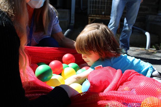 A young boy dives into a large red fabric bag filled with colourful plastic balls.