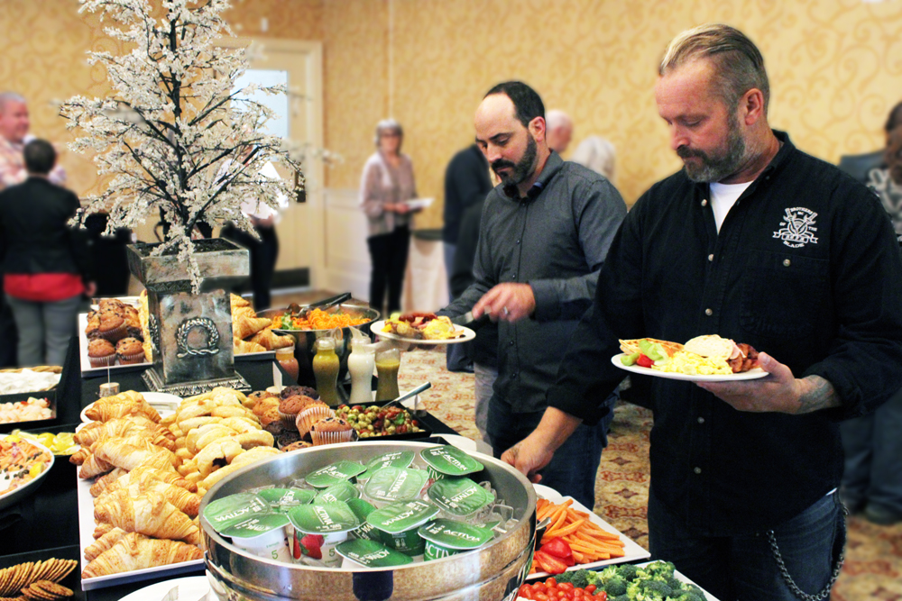 2 men holding white plates at a buffet table.