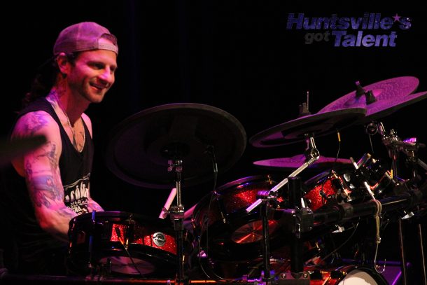 a smiling man seated at a drum kit.