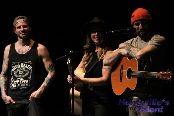 2 men and 1 woman, the Top 3 finalists, stand on stage waiting for the judges' results.