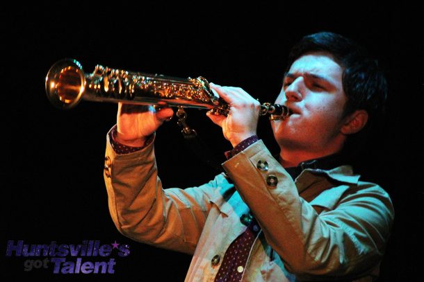 a young man playing a soprano saxophone leans back and lifts the saxophone to point its bell toward the audience.