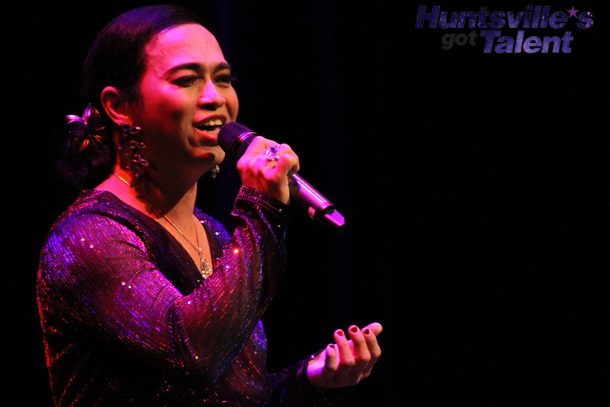 a singer in a purple ballgown sings into a microphone.