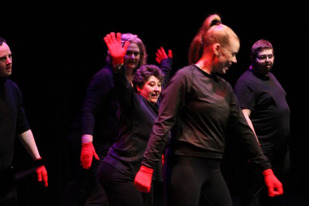 5 dancers dressed in black clothes and red gloves.